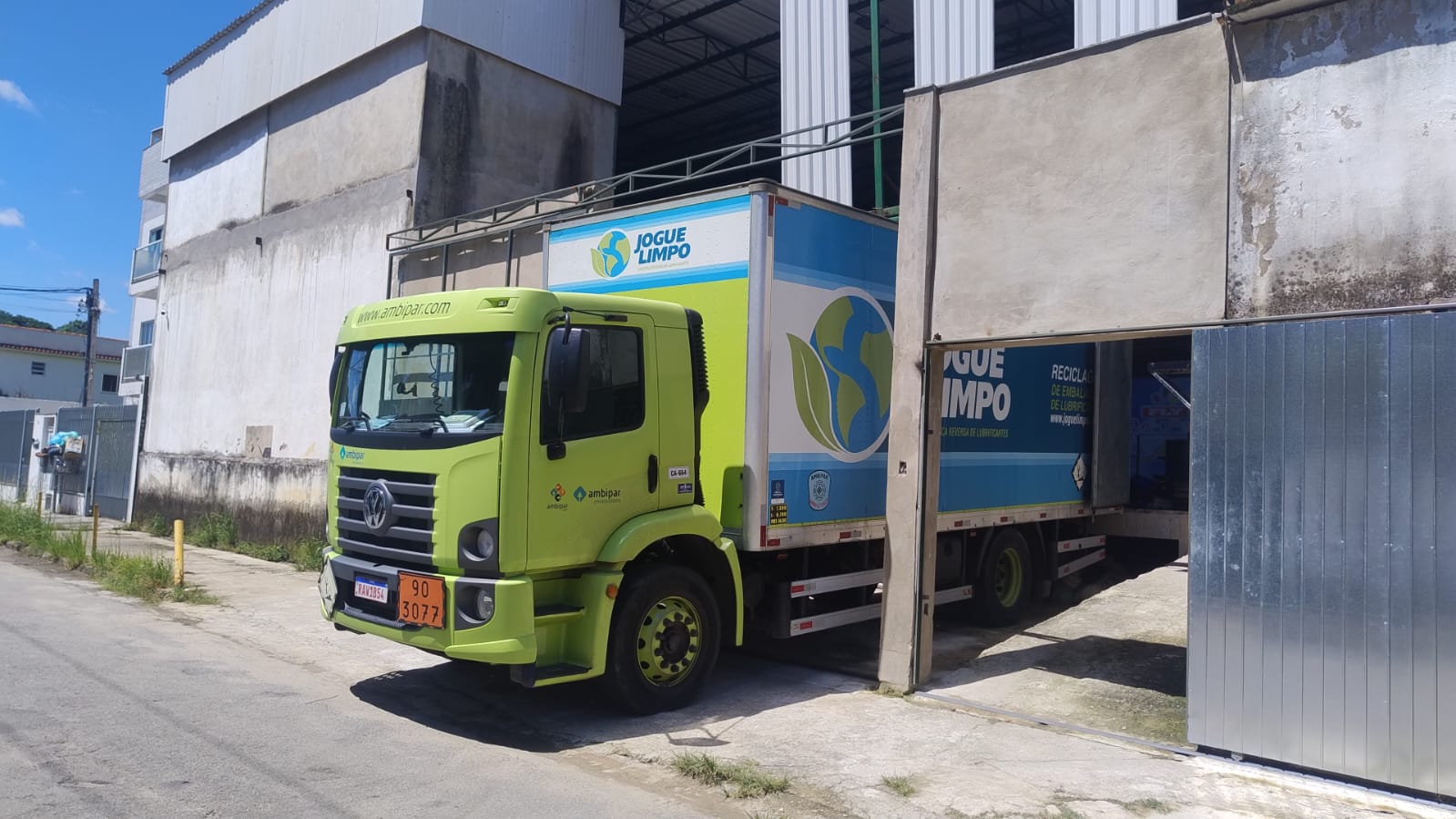 Caminhão da Ambipar, com o logotipo Ambipar visível, estacionado na fábrica da Fly Balloon para coleta de resíduos